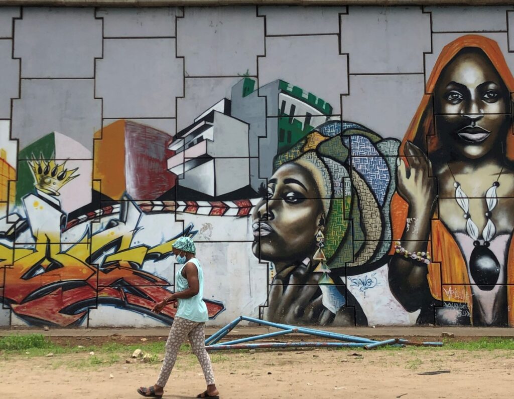 A woman walking by a wall mural in Senegal